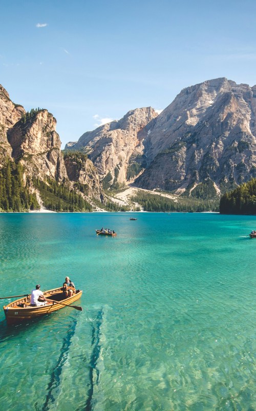 A few rewing boats on a turquoise lake surrounded by mountains