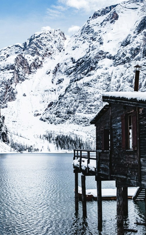 Wooden hut on stilts in the water of a lake, snow-covered mountain in the background