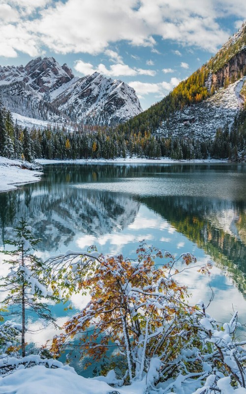 Snow-covered mountain landscape with lake, forest and rock faces
