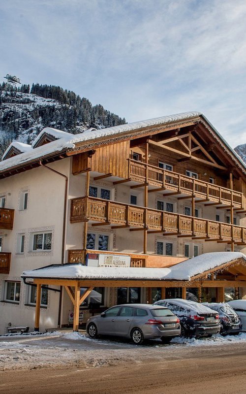 House with wooden balconies & cars in front of mountains with snow