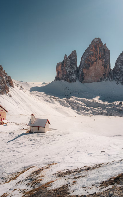Hut and small church in a snowy landscape surrounded by Dolomites peaks